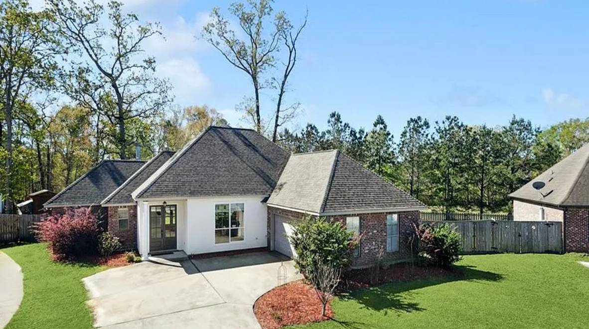 A house with a large driveway and trees in the background.